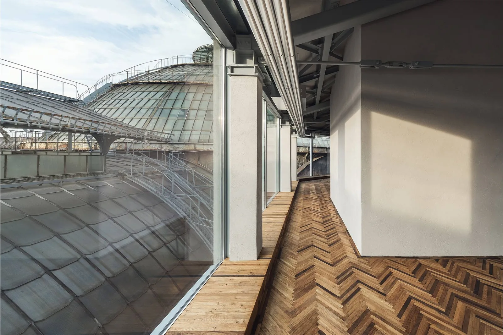 Prada Galleria: pasillo con parquet en espiga en una planta superior y, tras el ventanal, la bóveda de cristal de la galería