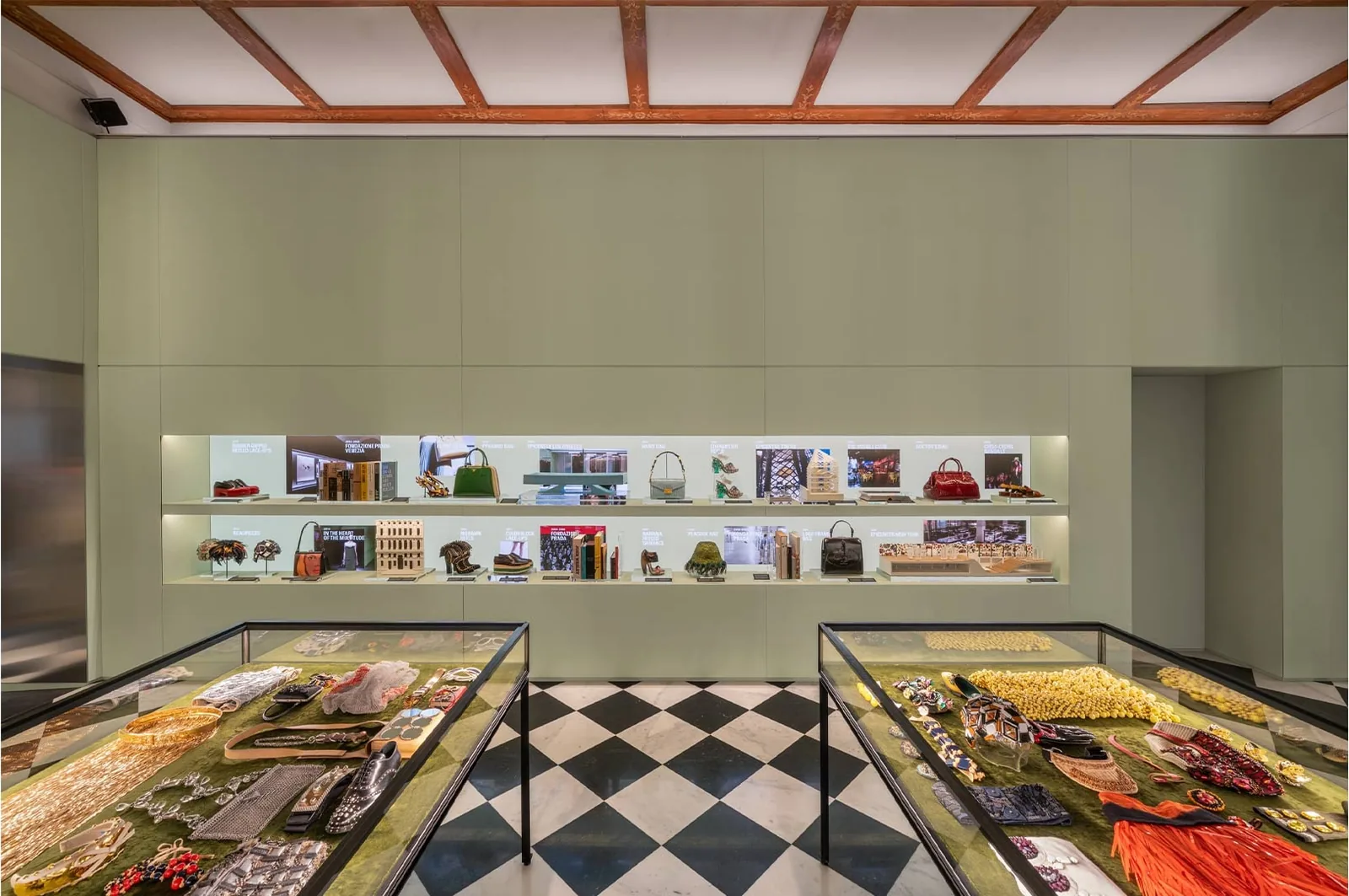Prada Galleria: sala de exposición con paredes verde salvia, estantes iluminados con bolsos y zapatos y vitrinas con joyas y accesorios