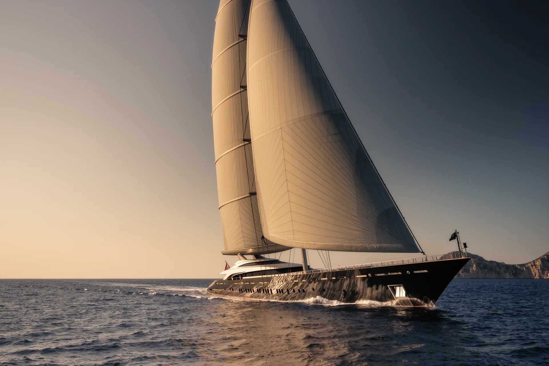 Velero de lujo de gran eslora navegando al atardecer con las velas de carbono desplegadas