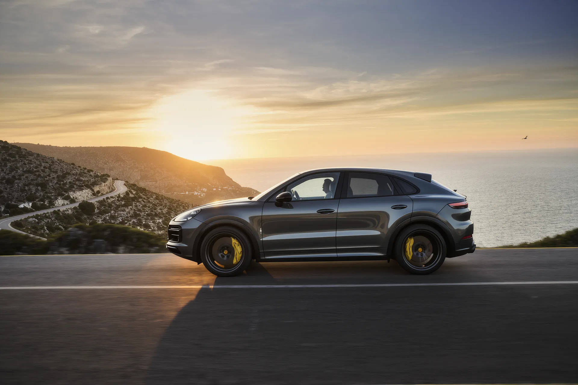 SUV de lujo deportivo en color gris grafito fotografiado de perfil sobre una carretera de montaña al atardecer