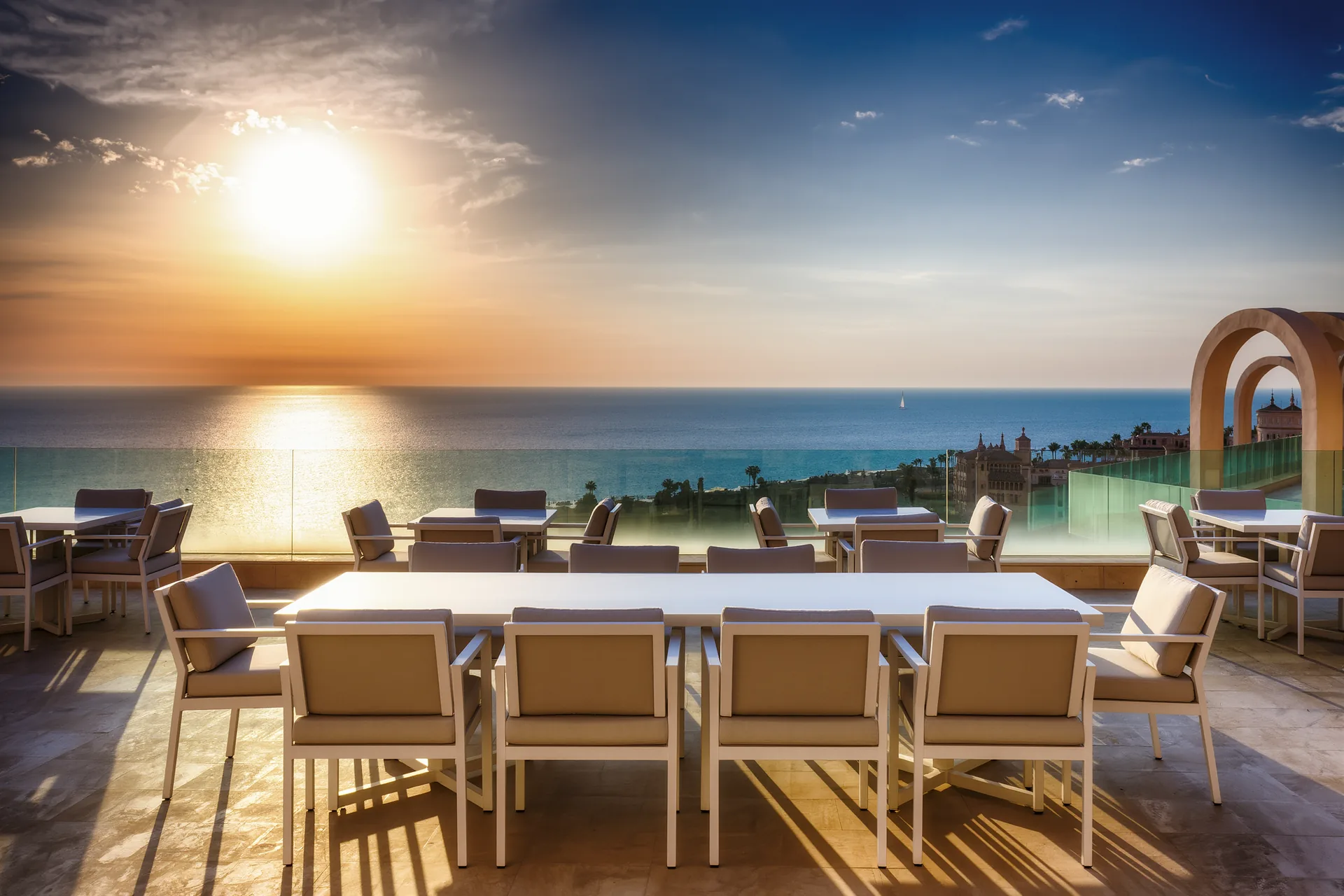 Terraza de un hotel de lujo frente al mar en un atardecer de otoño, completamente vacía de turistas, con mesas puestas y luz dorada baja
